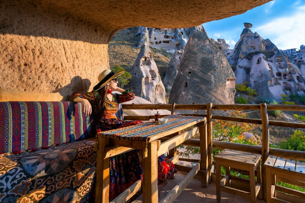 Woman In Bohemian Dress Sitting On Traditional Cave House In Cap